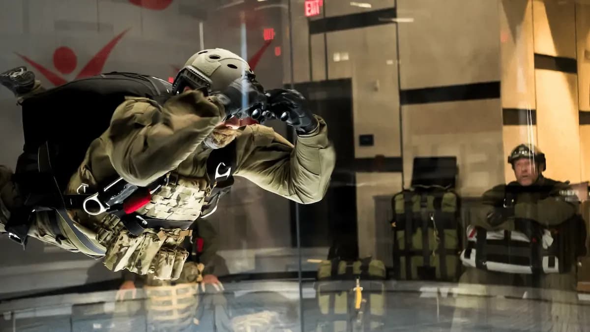 Soldier in full tactical gear flying in an indoor wind tunnel during training.