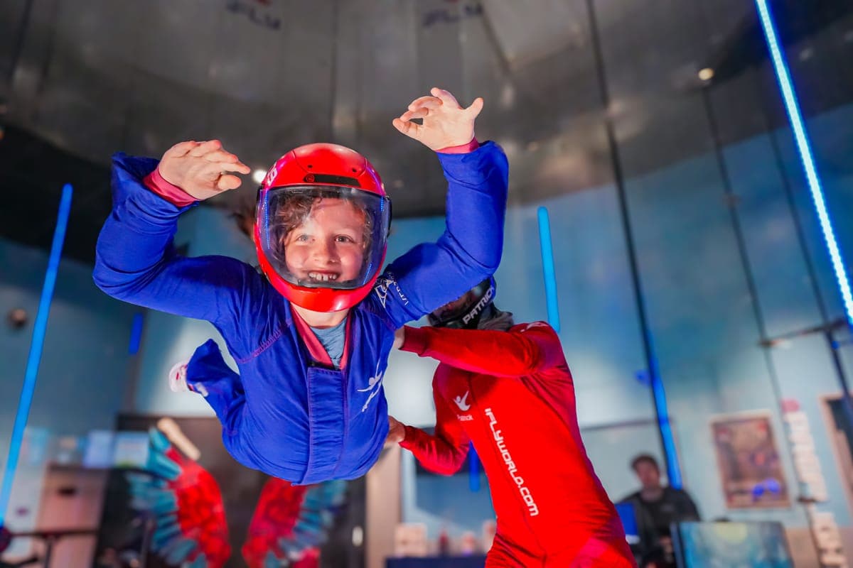 A young flyer in a blue suit and red helmet mid-flight in the wind tunnel