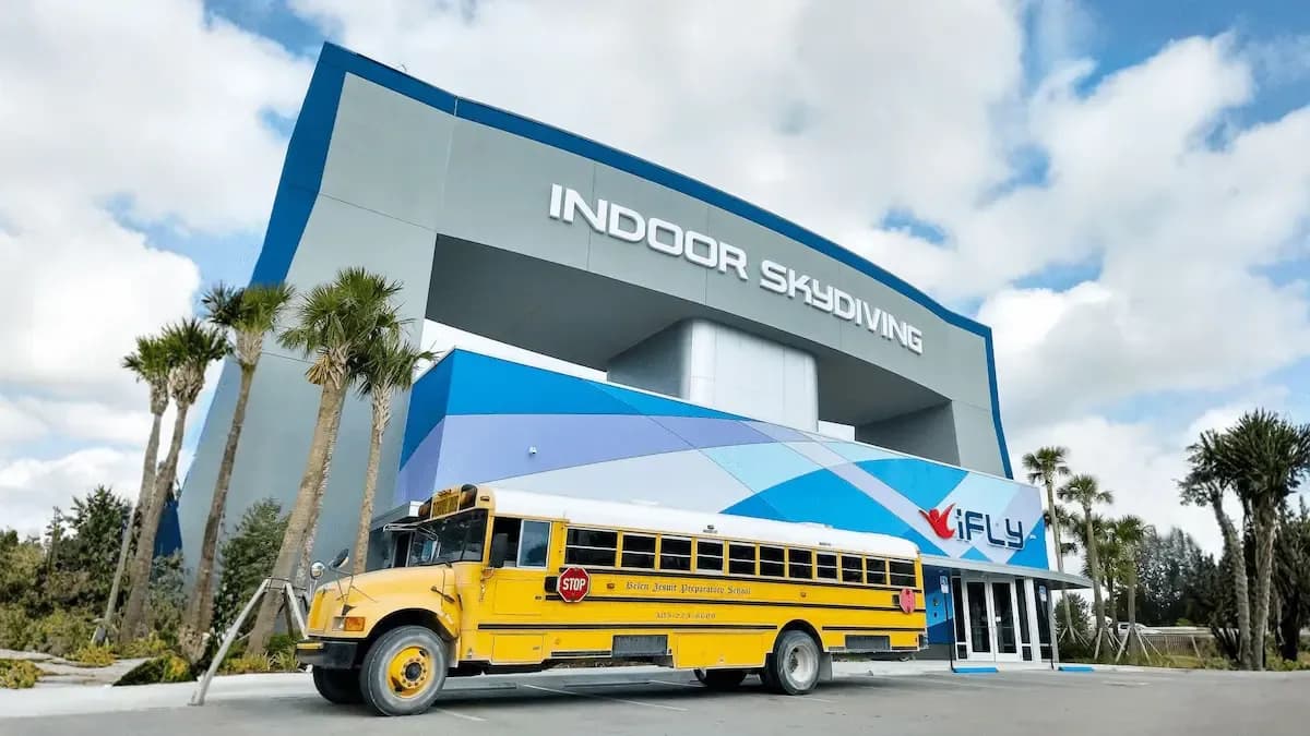 A yellow school bus parked outside a modern building with 'INDOOR SKYDIVING' written on it.